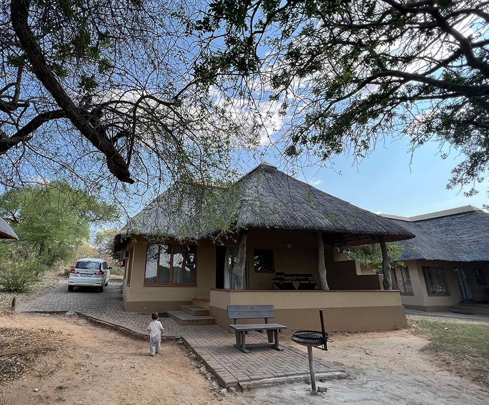 Casa de techo de paja en un campamento del Kruger, con porche, barbacoa y el coche aparcado a la sombra