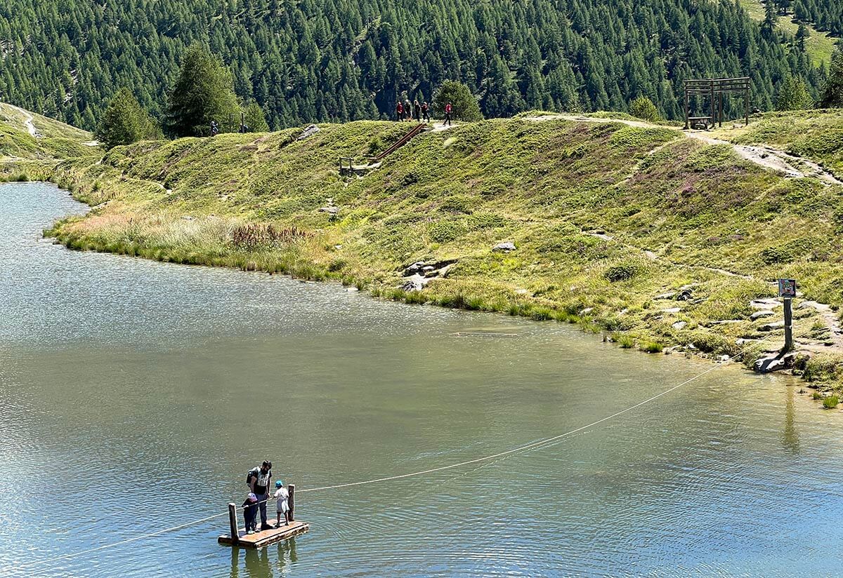 a man and two children crossing Sunnegga lake in Switzerland on a rope raft