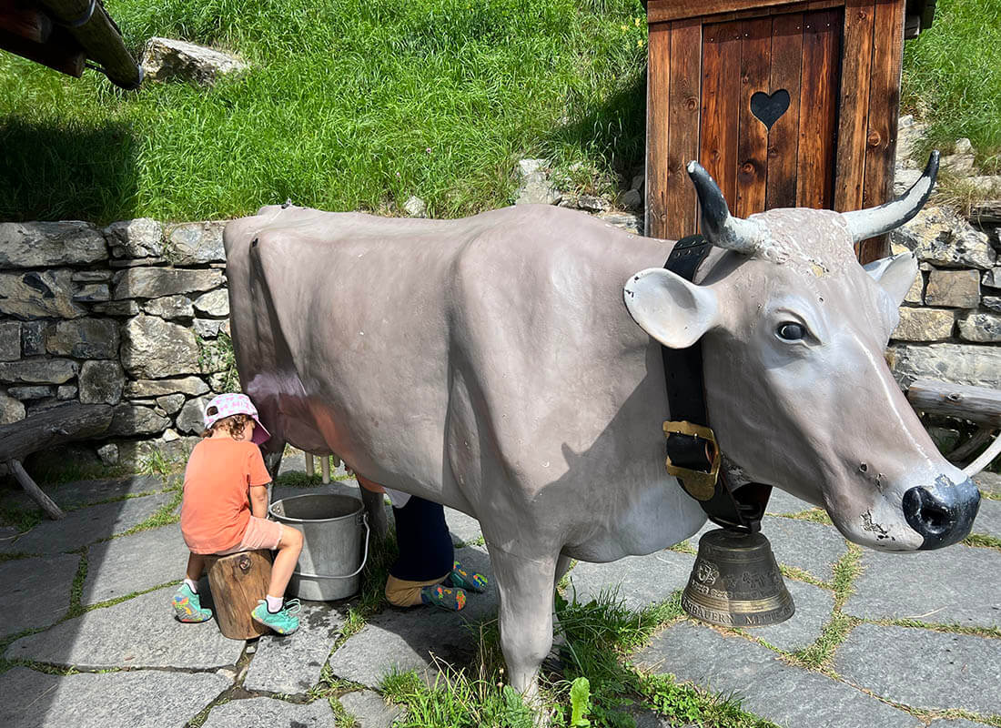 una niña simulando ordeñar una vaca en el pueblo de Heidi en Suiza