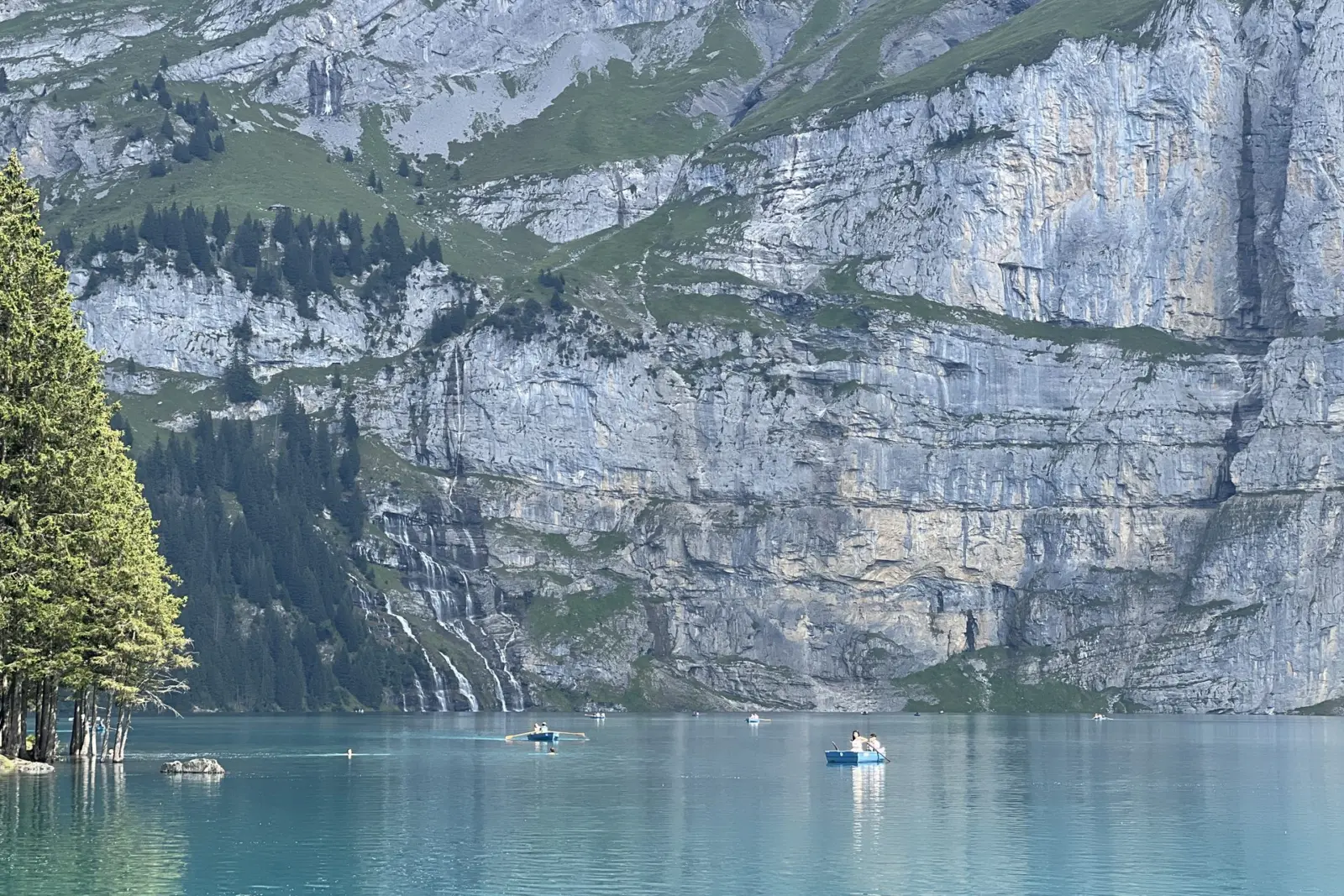 Barcas de remos bajo las paredes de roca y las cascadas del Oeschinensee