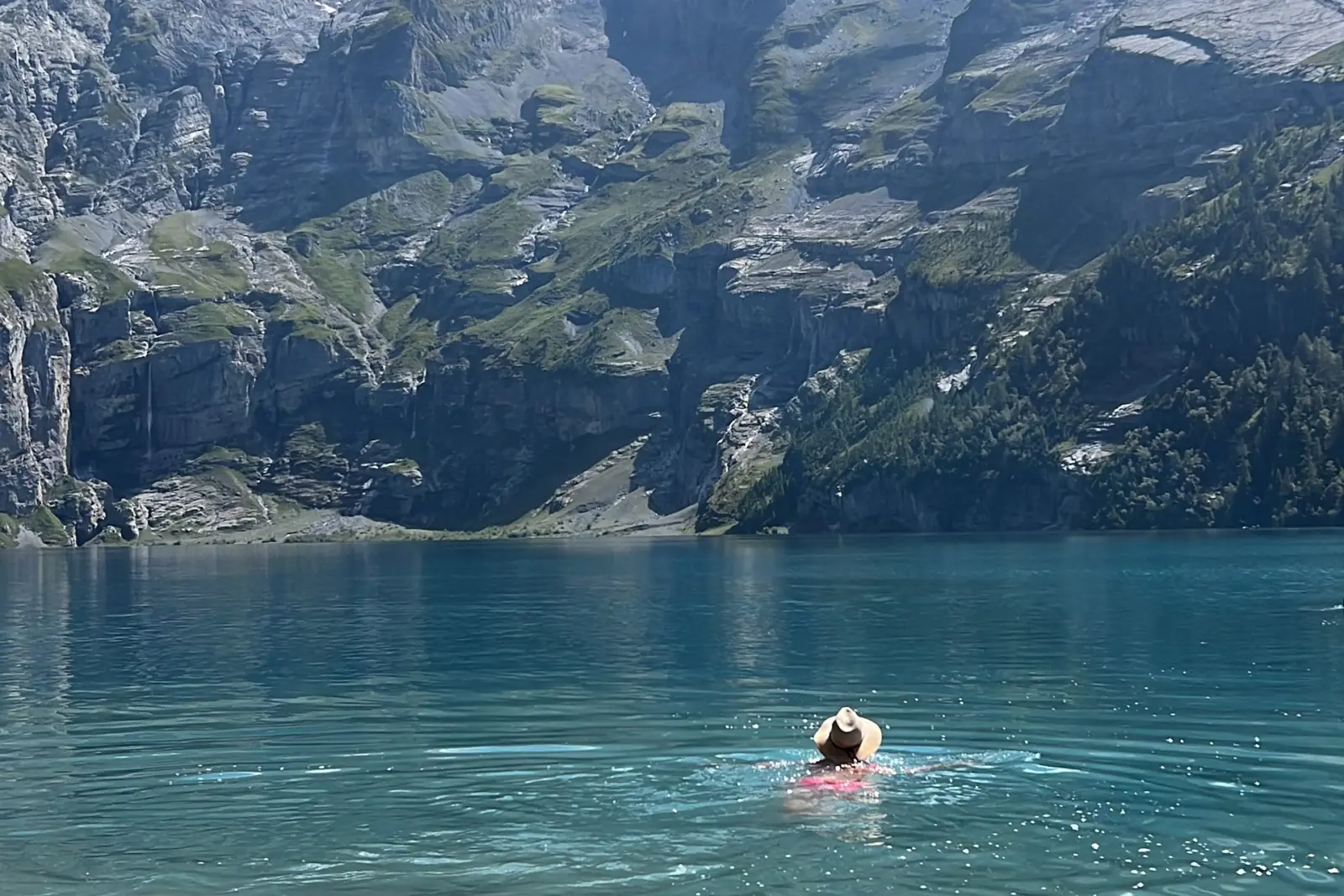Mujer con sombrero nadando en el agua turquesa y fría del Oeschinensee